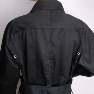 May include: A black long-sleeved jacket with a belt and a collar. The jacket has two pockets on the front and two eyelets on each sleeve.