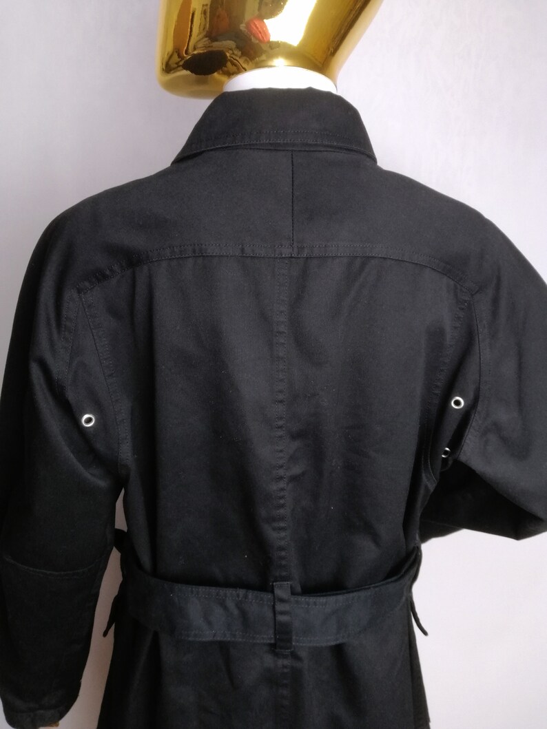 May include: A black long-sleeved jacket with a belt and a collar. The jacket has two pockets on the front and two eyelets on each sleeve.