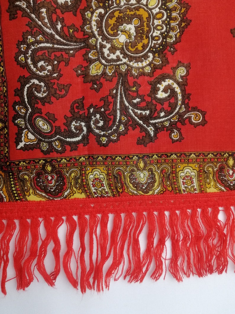 K&ouml;nnte beinhalten: Roter Schal mit Paisley-Muster und Fransenbord&uuml;re. Der Schal hat ein florales Design mit braunen, gelben und wei&szlig;en Akzenten.