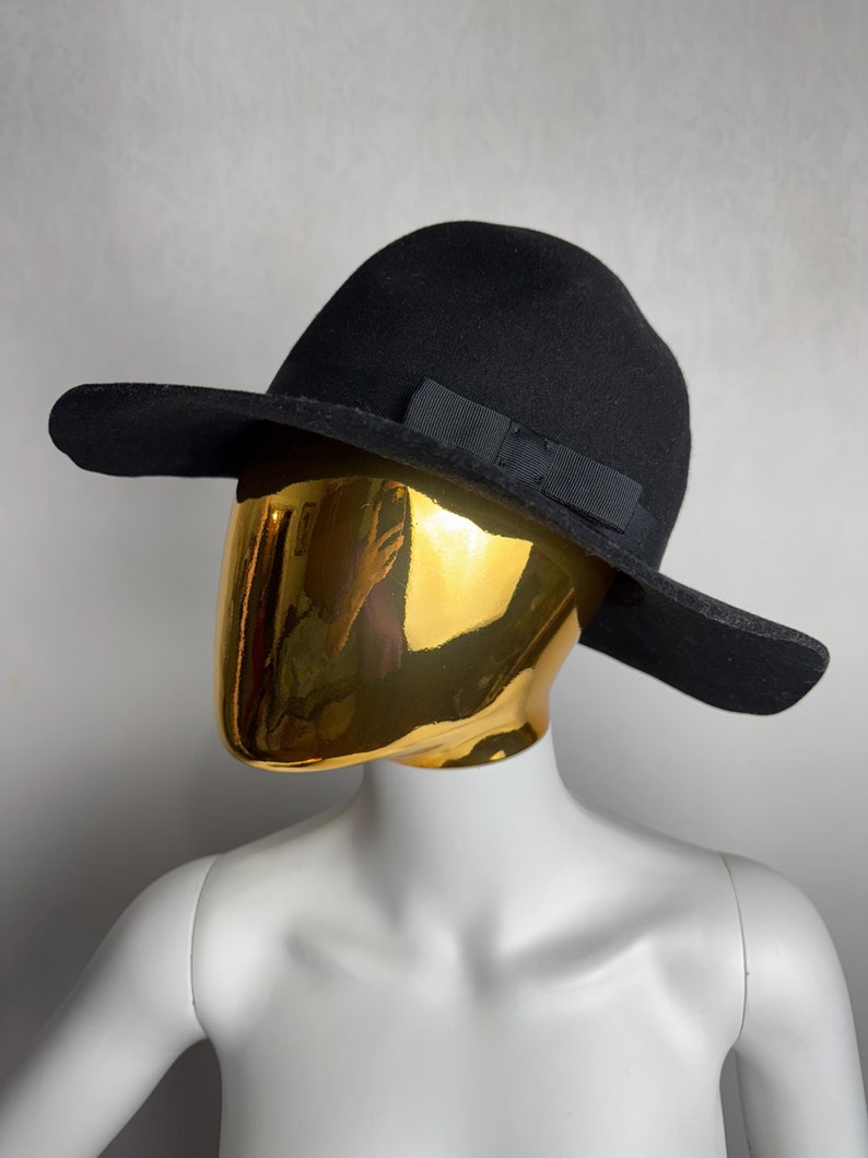 Puede incluir: Un sombrero de fieltro negro de ala ancha con un lazo de grosgrain negro.