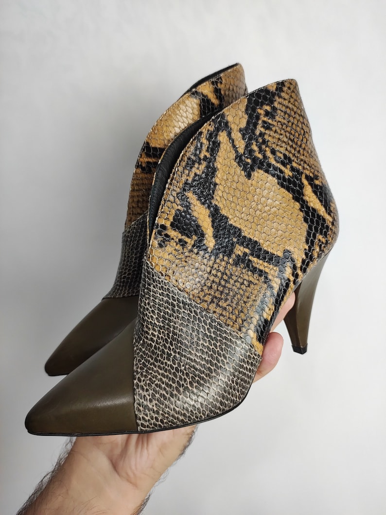 May include: A pair of brown and black snakeskin heeled ankle boots with a pointed toe.