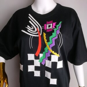 May include: Black t-shirt with a colourful geometric design embroidered on the front. The design features white, red, yellow, green, purple and pink.