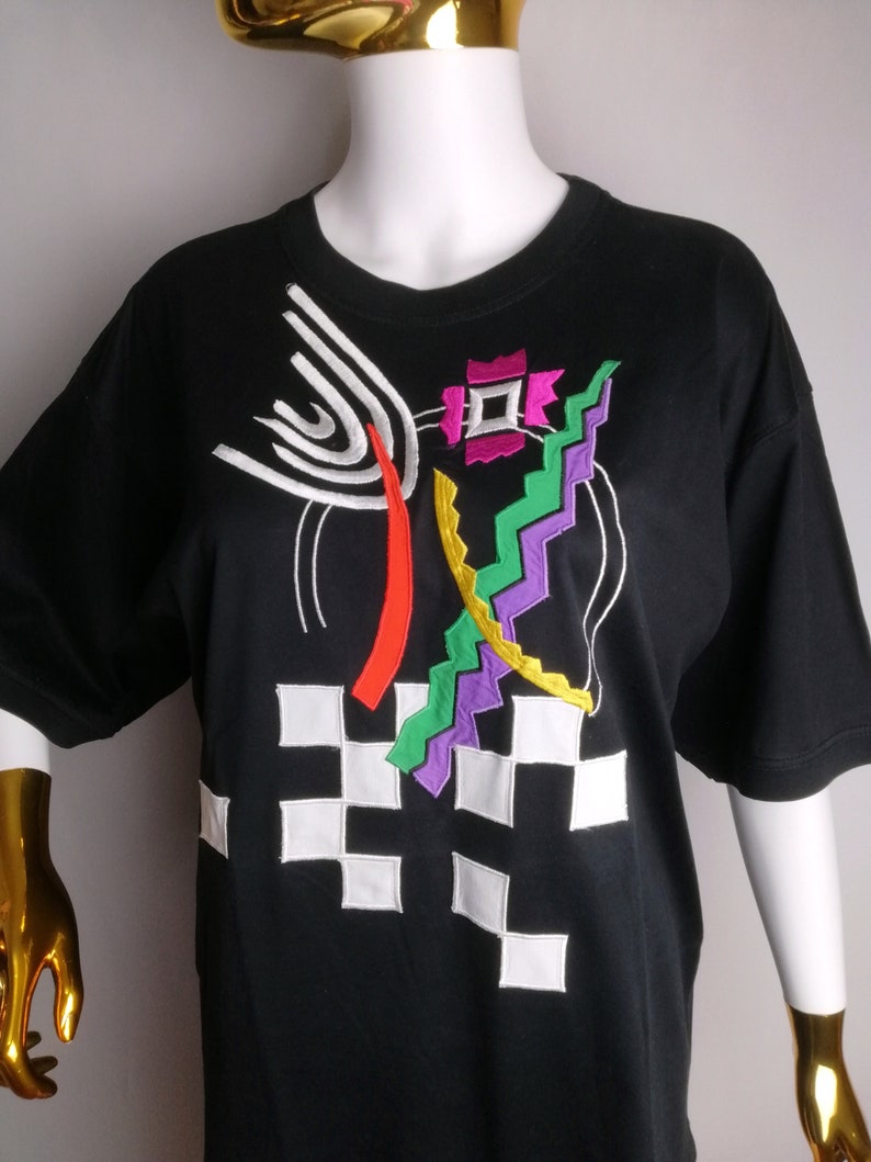 May include: Black t-shirt with a colourful geometric design embroidered on the front. The design features white, red, yellow, green, purple and pink.