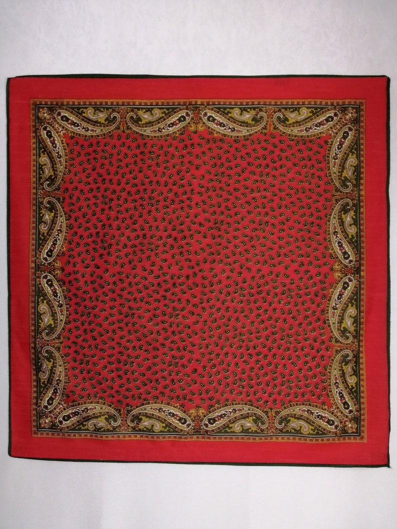 Puede incluir: Un pa&ntilde;uelo cuadrado rojo con borde negro y estampado de cachemira. El centro del pa&ntilde;uelo est&aacute; cubierto de peque&ntilde;as formas de cachemira oscuras. El borde presenta dise&ntilde;os de cachemira m&aacute;s grandes en dorado, negro y blanco.