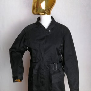 May include: A black utility jacket with a belted waist, multiple pockets, and a stand-up collar.