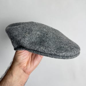Pode incluir: Bon&eacute; plano cinzento de l&atilde;. O chap&eacute;u tem uma coroa arredondada e uma aba pequena e r&iacute;gida. O bon&eacute; &eacute; segurado contra um fundo branco.