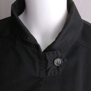 May include: A black collared jacket with a single button closure. The jacket has a slightly angled collar and a smooth, cotton-like texture.