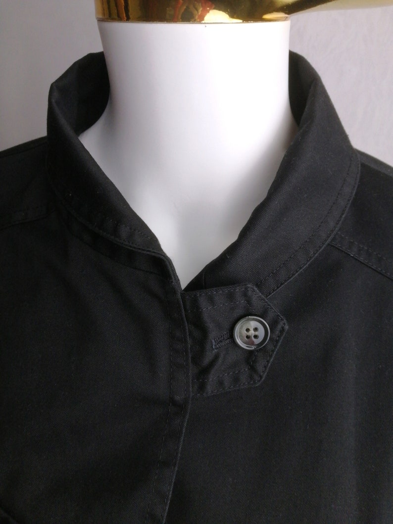May include: A black collared jacket with a single button closure. The jacket has a slightly angled collar and a smooth, cotton-like texture.
