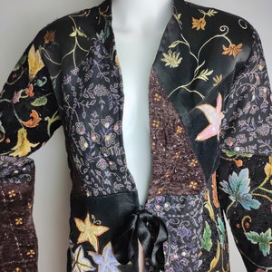 May include: A black jacket with a floral pattern and a tie at the waist. The jacket is made of different fabrics and has a patchwork design.