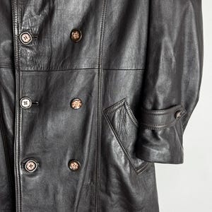 May include: A dark brown leather coat with a double-breasted design. The coat features multiple buttons, a notched collar, and a tailored fit. The coat has a classic, vintage style, with a pocket on the front.