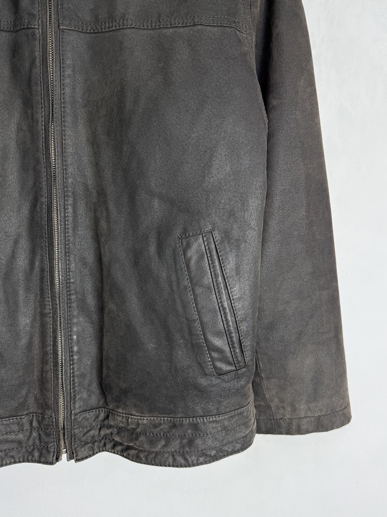 Puede incluir: Chaqueta de cuero marr&oacute;n oscuro con cierre de cremallera y un peque&ntilde;o bolsillo en el pecho. La chaqueta tiene un aspecto desgastado y texturizado y un dise&ntilde;o cl&aacute;sico. La chaqueta es de peso medio y adecuada para climas m&aacute;s fr&iacute;os.