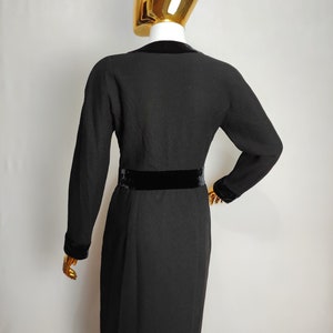 K&ouml;nnte beinhalten: Schwarzes Kleid mit langen &Auml;rmeln und einem Samtg&uuml;rtel. Das Kleid hat eine figurbetonte Silhouette und einen V-Ausschnitt.