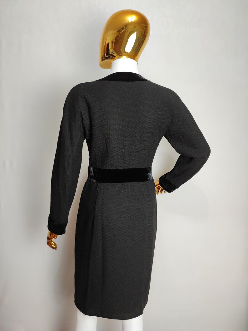 K&ouml;nnte beinhalten: Schwarzes Kleid mit langen &Auml;rmeln und einem Samtg&uuml;rtel. Das Kleid hat eine figurbetonte Silhouette und einen V-Ausschnitt.