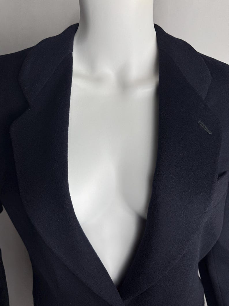 Pode incluir: Um blazer azul escuro com uma gola em V profunda e um fecho de um &uacute;nico bot&atilde;o.