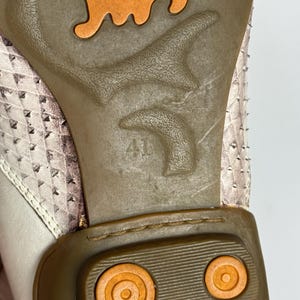 K&ouml;nnte beinhalten: Nahaufnahme der Schuhsohle. Die braune Gummisohle hat ein orangefarbenes Design und die Zahl 41. Das Obermaterial des Schuhs ist ein hellrosa und wei&szlig; gemustertes Material.
