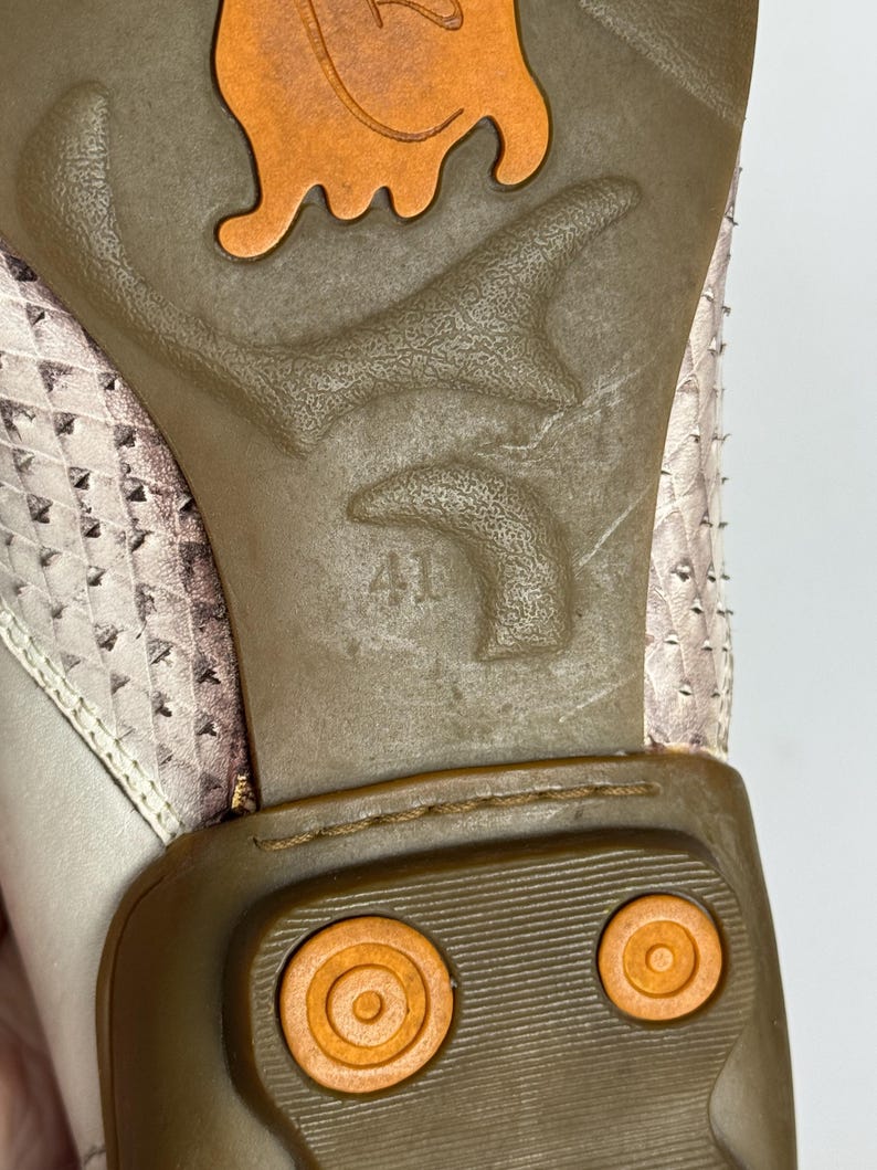 K&ouml;nnte beinhalten: Nahaufnahme der Schuhsohle. Die braune Gummisohle hat ein orangefarbenes Design und die Zahl 41. Das Obermaterial des Schuhs ist ein hellrosa und wei&szlig; gemustertes Material.