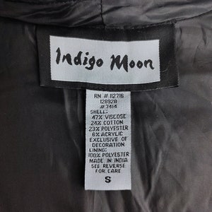 May include: A white tag with black text that reads "Indigo Moon" and lists the fabric content and care instructions for a garment. The tag also includes the RN number, style number, and size "S".