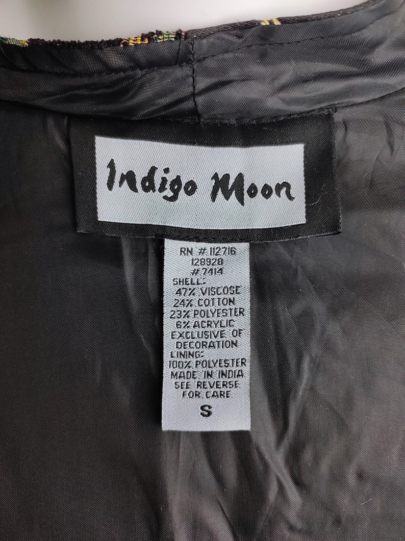 May include: A white tag with black text that reads "Indigo Moon" and lists the fabric content and care instructions for a garment. The tag also includes the RN number, style number, and size "S".