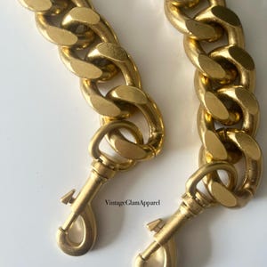 May include: Two gold-toned chain straps with lobster claw clasps. The chains are thick and have a chunky, curb link design.