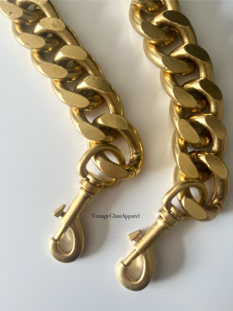 May include: Two gold-toned chain straps with lobster claw clasps. The chains are thick and have a chunky, curb link design.