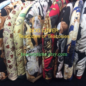 May include: A collection of 10 colourful tea cosies featuring various dog breeds. The cosies are made of fabric with a dog-themed print. The text "DOG LOVER Teacozies or Teacosies teacozytime.etsy.com" is printed on the cosies.