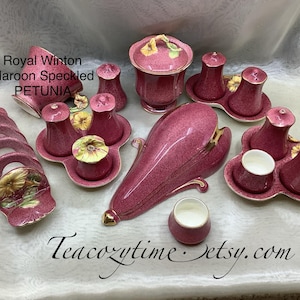 Könnte beinhalten: Ein Royal Winton Maroon Speckled Petunia Porzellanset. Das Set beinhaltet eine Schüssel mit Deckel, Salz- und Pfefferstreuer, einen Sahnekännchen und eine Servierschale. Die Teile sind weinrot mit goldenen Akzenten und floralen Details.