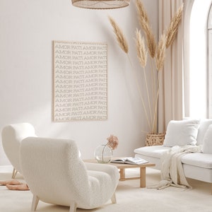 May include: A white living room with a white couch, two white fluffy chairs, a wooden coffee table, a vase with pink flowers, a wicker basket, and a framed print with the text "AMOR PATI AMOR PATI" repeated multiple times.