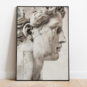 May include: Black and white framed print of a classical sculpture head. The sculpture is weathered, with visible cracks and imperfections, set against a white background. The artwork is a profile view of a male figure.