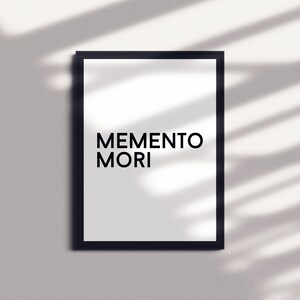 May include: A black framed print with the text "MEMENTO MORI" in white letters on a white background.