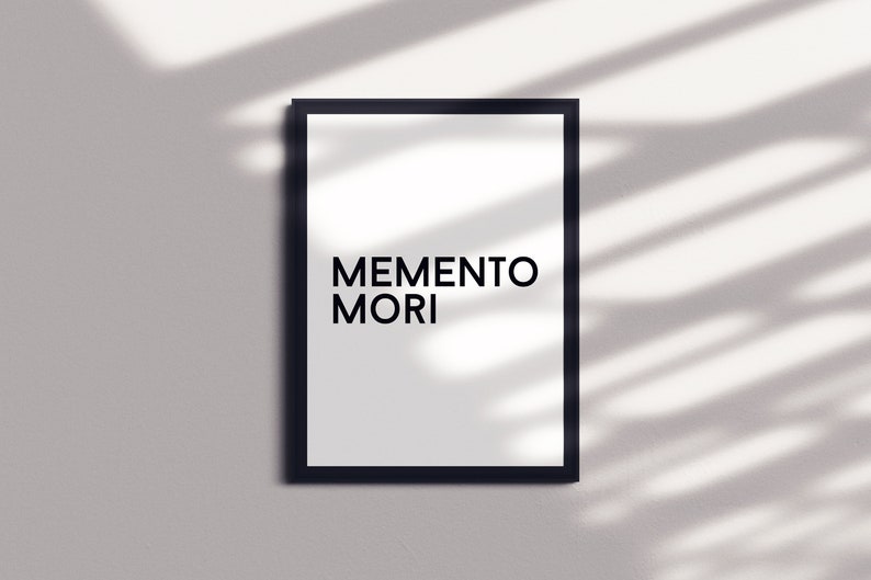 May include: A black framed print with the text "MEMENTO MORI" in white letters on a white background.