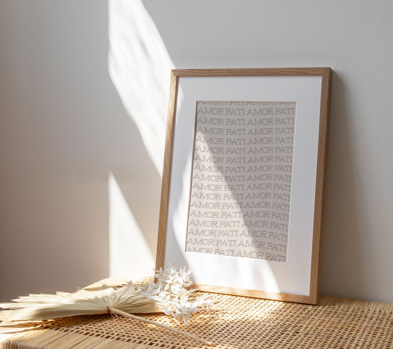 May include: A framed print with the words "AMOR PATI" repeated in a vertical pattern on a white background. The frame is light brown wood.