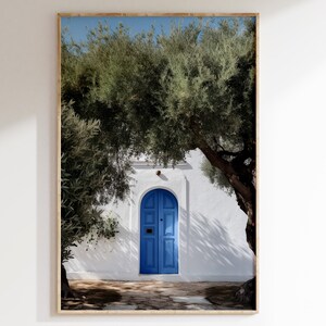 Peut inclure: Impression encadr&eacute;e d'une porte bleue vive encastr&eacute;e dans un mur en stuc blanc, encadr&eacute;e d'oliviers verdoyants. La lumi&egrave;re du soleil cr&eacute;e des ombres marqu&eacute;es. L'image &eacute;voque une esth&eacute;tique m&eacute;diterran&eacute;enne.