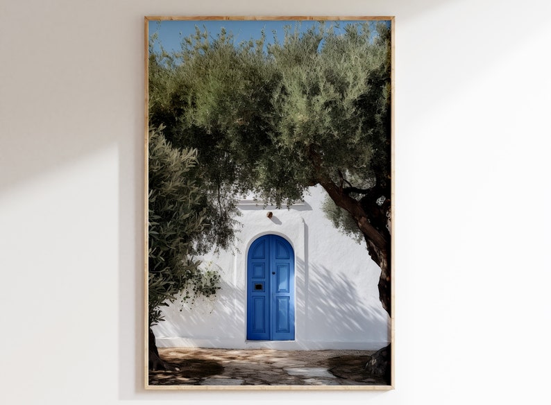 Peut inclure: Impression encadr&eacute;e d'une porte bleue vive encastr&eacute;e dans un mur en stuc blanc, encadr&eacute;e d'oliviers verdoyants. La lumi&egrave;re du soleil cr&eacute;e des ombres marqu&eacute;es. L'image &eacute;voque une esth&eacute;tique m&eacute;diterran&eacute;enne.