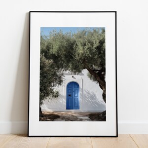 Peut inclure: Tirage encadr&eacute; d'une porte bleue vive encastr&eacute;e dans un mur blanc, encadr&eacute;e par un feuillage vert luxuriant. L'image capture une journ&eacute;e ensoleill&eacute;e avec des ombres et un ciel bleu clair, &eacute;voquant une esth&eacute;tique m&eacute;diterran&eacute;enne.
