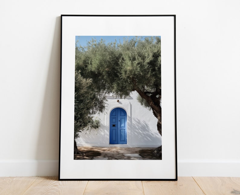 Peut inclure: Tirage encadr&eacute; d'une porte bleue vive encastr&eacute;e dans un mur blanc, encadr&eacute;e par un feuillage vert luxuriant. L'image capture une journ&eacute;e ensoleill&eacute;e avec des ombres et un ciel bleu clair, &eacute;voquant une esth&eacute;tique m&eacute;diterran&eacute;enne.