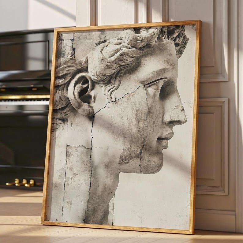 May include: A framed black and white print of a classical sculpture bust. The artwork features a detailed profile of a male figure with curly hair and a cracked, aged appearance. The frame is a light brown color.