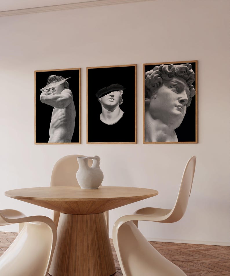 K&ouml;nnte beinhalten: Drei gerahmte Schwarzwei&szlig;drucke von klassischen Skulpturen. Die Drucke h&auml;ngen an einer wei&szlig;en Wand &uuml;ber einem Holztisch mit zwei beigen St&uuml;hlen.