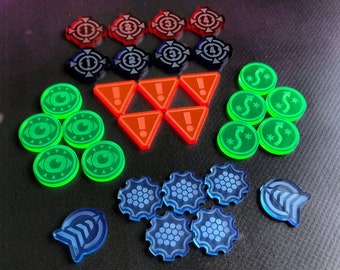 May include: A set of colorful game pieces in various shapes and designs. The pieces are made of acrylic and feature different symbols and numbers. The set includes green, blue, red, and black pieces.