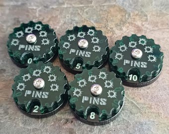 May include: Five dark green game tokens with the word "PINS" and numbers 0, 2, 5, 8, and 10. Each token has a silver center and a decorative pattern around the edge.