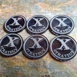 May include: Six black and silver round tokens with the word "STRATEGY" and a stylized "X" printed on each.