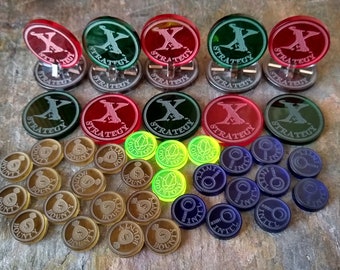 May include: A set of game pieces for a strategy game. The pieces are made of clear plastic and feature different colors and designs. There are red, green, and black pieces with the word "STRATEGY" printed on them. There are also gold, green, and blue tokens with different designs.