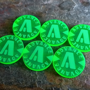Puede incluir: Seis fichas de plástico verde brillante con la palabra "ADVANCE" escrita alrededor del borde y una letra "A" estilizada en el centro.