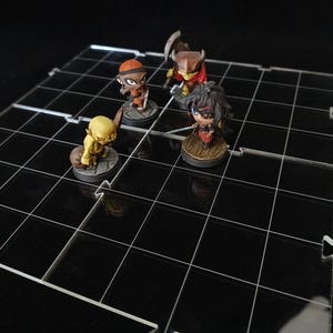 May include: A clear acrylic grid-based game board with four miniature figurines. The board has a black grid pattern. The figurines are of various colors and designs, suggesting a tabletop role-playing game.
