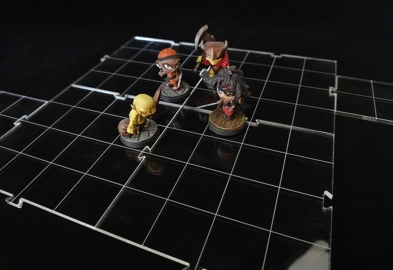 May include: A clear acrylic grid-based game board with four miniature figurines. The board has a black grid pattern. The figurines are of various colors and designs, suggesting a tabletop role-playing game.