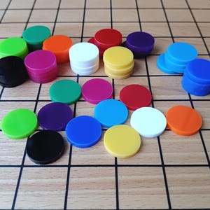 Puede incluir: Un conjunto de piezas de juego coloridas, verdes, naranjas, rojas, amarillas, azules, moradas, rosas, blancas y negras. Dispuestas sobre un tablero de madera con un patrón de cuadrícula, para juegos de mesa.