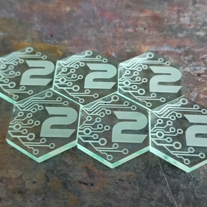 Könnte beinhalten: Sechs durchsichtige, grüne, sechseckige Spielsteine mit einem Leiterplatten-Design und der Zahl "2" auf jeder Seite.