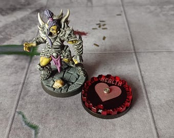 May include: A green and gray miniature figure of a warrior with a purple sash and horns. The figure is standing on a round, gray base. A red and black health tracker with a heart symbol and the word "HEALTH" is in the foreground.