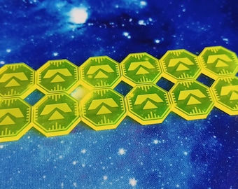 May include: A set of 14 yellow hexagonal game tokens with a green triangle symbol on each. The tokens are arranged in two rows.
