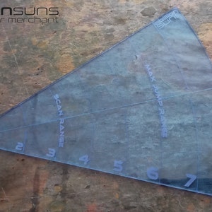 Peut inclure: Un rapporteur en plastique bleu transparent avec des marques pour "SCAN RANGE" et "MAX JUMP RANGE". Le rapporteur comporte les chiffres de 1 à 8 le long du bord inférieur.