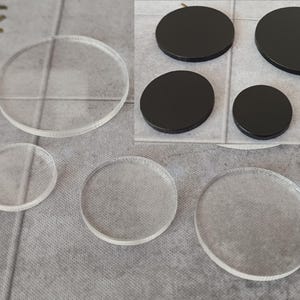 May include: A selection of clear and black circular items in different sizes. The clear items look like glass or acrylic. The black items have a matte finish. The items are displayed on a grey surface.